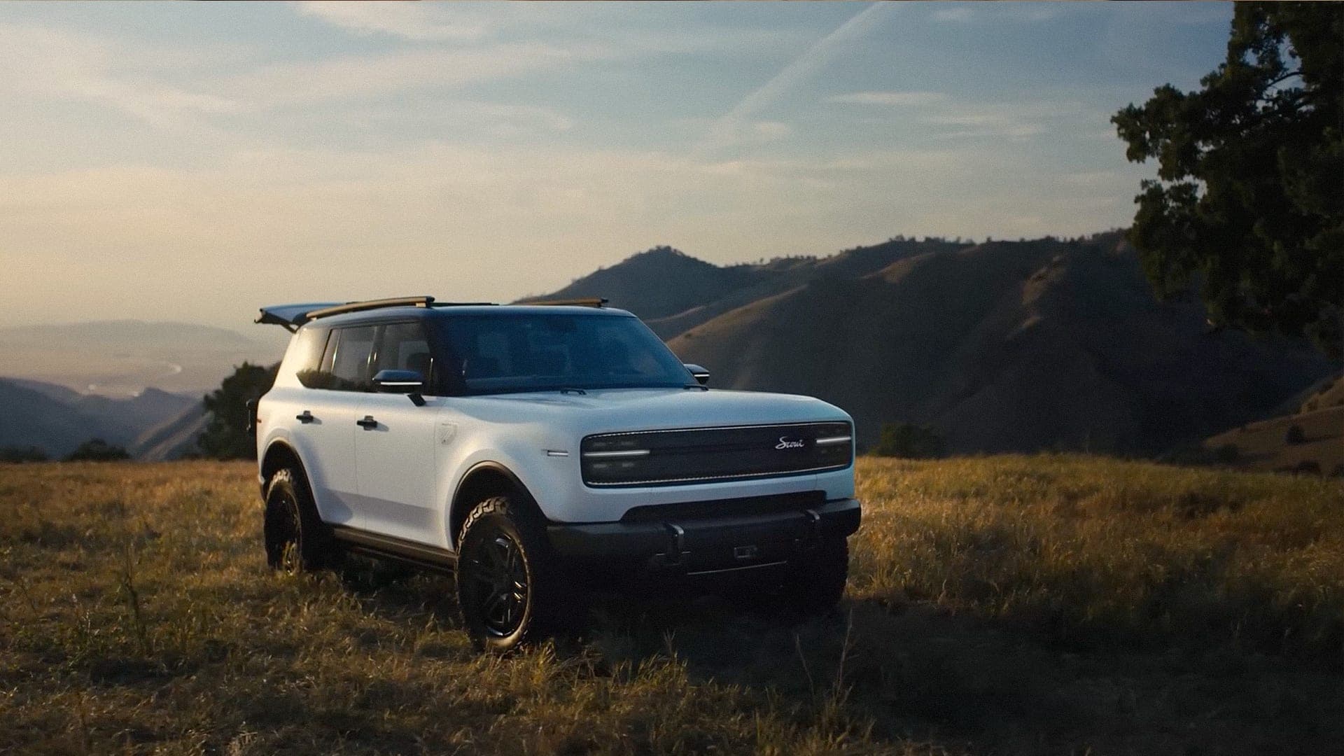 A white SUV parked on a dry golden ridge at dusk, hills falling away behind it
